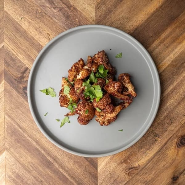 Crispy roasted cauliflower florets garnished with fresh parsley on a gray plate, on a wooden table.