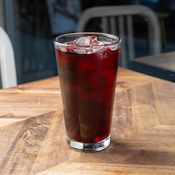 A tall glass of iced hibiscus tea sits on a wooden table with a blurred background.