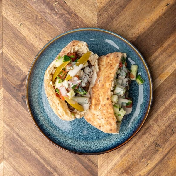 Two pita bread sandwiches filled with falafel, salad, pickles, and white sauce on a blue plate.